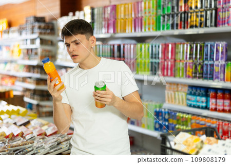 Young guy choosing colored drinks in drinks section of supermarket Young guy choosing colored drinks in drinks section of supermarket 109808179