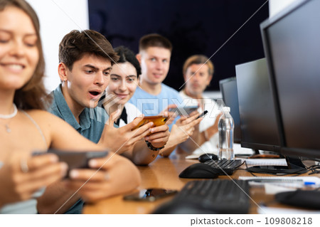 At computer class, young guy student sits with mobile phone and listens admiringly to teacher At computer class, young guy student sits with mobile phone and listens admiringly to teacher 109808218