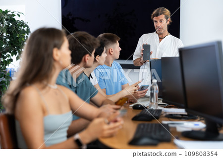 During computer courses, male teacher with mobile phone explains to listeners principle of operation 109808354