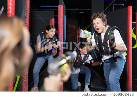 Emotional man with laser pistol playing laser tag with friends on dark labyrinth Emotional man with laser pistol playing laser tag with friends on dark labyrinth 109808456