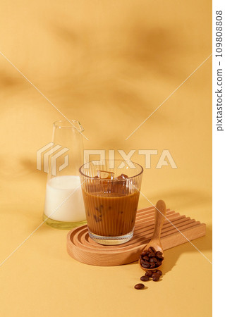 A glass of milk coffee and a wooden spoon with coffee beans are displayed on a wooden platform. Caffeine in coffee has the ability to burn fat and effectively support weight loss. A glass of milk coffee and a wooden spoon with coffee beans are displayed on a wooden platform. Caffeine in coffee has the ability to burn fat and effectively support weight loss. 109808808