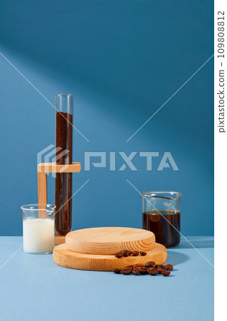 The wooden platform is placed in the center of the frame, next to it is a cup of milk, a cup of black coffee, coffee beans and coffee powder in a test tube with a blue background. The wooden platform is placed in the center of the frame, next to it is a cup of milk, a cup of black coffee, coffee beans and coffee powder in a test tube with a blue background. 109808812