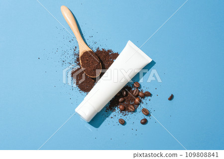 Top view of an unlabeled white tube, coffee powder, coffee beans and a spoon on a blue background. Clean skin with coffee grounds. Natural ingredients are good for the skin. Top view of an unlabeled white tube, coffee powder, coffee beans and a spoon on a blue background. Clean skin with coffee grounds. Natural ingredients are good for the skin. 109808841