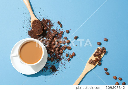 A glass of milky coffee is placed next to coffee beans and coffee powder on a blue background. Coffee helps block chemicals that cause muscle fatigue during intense physical activities. A glass of milky coffee is placed next to coffee beans and coffee powder on a blue background. Coffee helps block chemicals that cause muscle fatigue during intense physical activities. 109808842