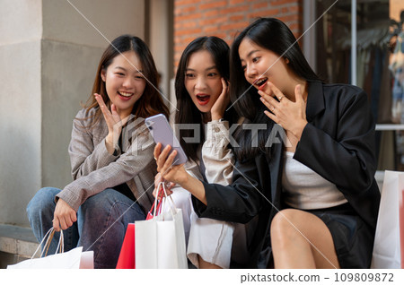 Excited female friends are looking at a phone screen with surprising faces, shocked with discount. 109809872