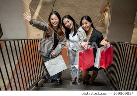 A group of attractive Asian female friends are carrying shopping bags, enjoying shopping together. A group of attractive Asian female friends are carrying shopping bags, enjoying shopping together. 109809884
