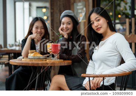 An attractive Asian woman in trendy clothes sitting at a table in a restaurant with her friends. An attractive Asian woman in trendy clothes sitting at a table in a restaurant with her friends. 109809903