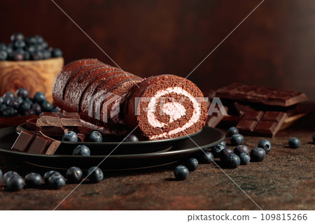 Chocolate roll cake with blueberries and a broken chocolate bar. 109815266