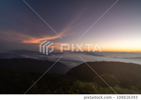 Early morning night sky from the top of Doi Luang Chiang Dao in Chiang Mai, Thailand overlooking a glowing town lights and beautiful dark blue sky with stars and glowing golden sun light at the 109816393
