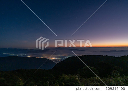 Early morning night sky from the top of Doi Luang Chiang Dao in Chiang Mai, Thailand overlooking a glowing town lights and beautiful dark blue sky with stars and glowing golden sun light at the 109816400