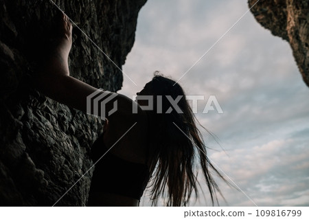 Sports Woman Climbing The Rock. Young woman With slim fit body climbing in volcanic basalt cave with beautiful sea view. The athlete girl trains in nature. Woman overcomes difficult climbing route. Sports Woman Climbing The Rock. Young woman With slim fit body climbing in volcanic basalt cave with beautiful sea view. The athlete girl trains in nature. Woman overcomes difficult climbing route. 109816799