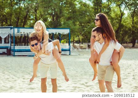 Group of friends walking along the beach, with men giving piggyback ride to girlfriends. Group of friends walking along the beach, with men giving piggyback ride to girlfriends. 109818512