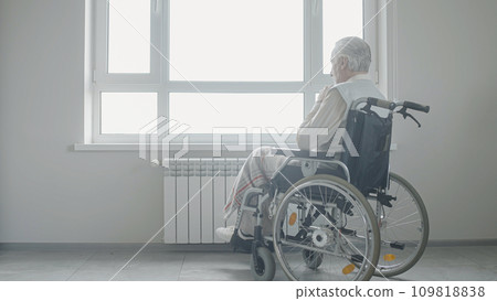 Sad senior man in wheelchair looking out the window, loneliness in old age Sad senior man in wheelchair looking out the window, loneliness in old age 109818838