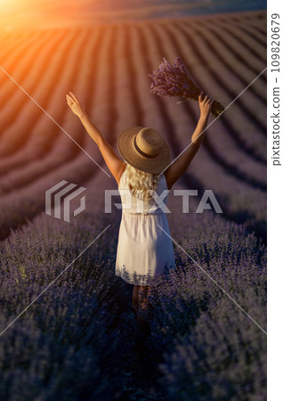 Blonde woman poses in lavender field at sunset. Happy woman in white dress holds lavender bouquet. Aromatherapy concept, lavender oil, photo session in lavender Blonde woman poses in lavender field at sunset. Happy woman in white dress holds lavender bouquet. Aromatherapy concept, lavender oil, photo session in lavender 109820679