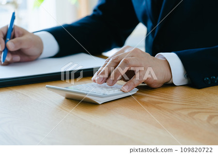 Hand of a man in a suit working on a calculator Hand of a man in a suit working on a calculator 109820722