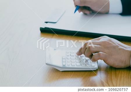 Hand of a man in a suit working on a calculator Hand of a man in a suit working on a calculator 109820737