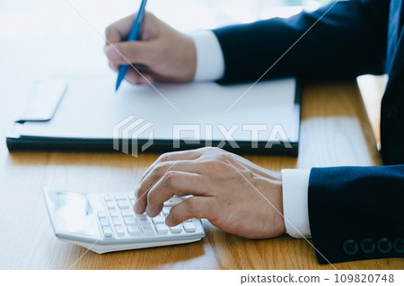 一個穿著西裝的男人的手在計算器上工作 109820748