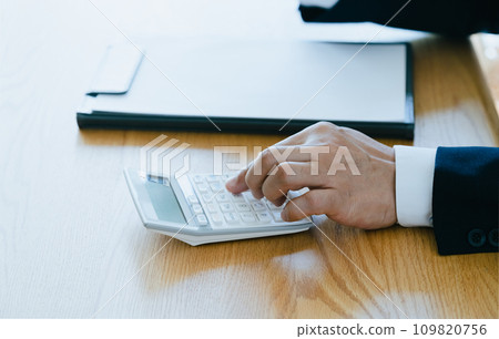 Hand of a man in a suit working on a calculator 109820756