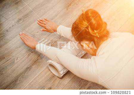 Adult athletic woman, in white bodysuit, performing fascia exercises on the floor - caucasian woman using a massage foam roller - a tool to relieve tension in the back and relieve muscle pain - the 109820821