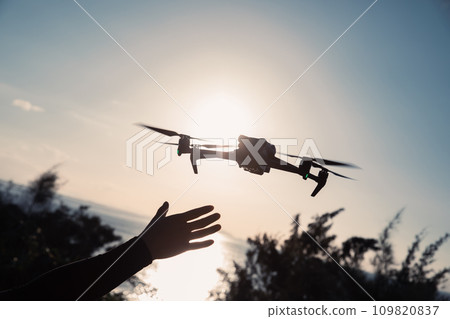 Silhouette of flying drone taking photo over sunrise Silhouette of flying drone taking photo over sunrise 109820837