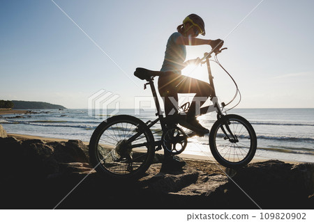 Riding folding bike on sunrise seaside road 109820902
