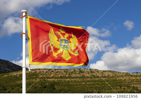 Flag of Montenegro waving in the wind with sky and mountains in background 109821956