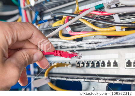 closeup of hand of administrator connecting network cable into switch 109822312