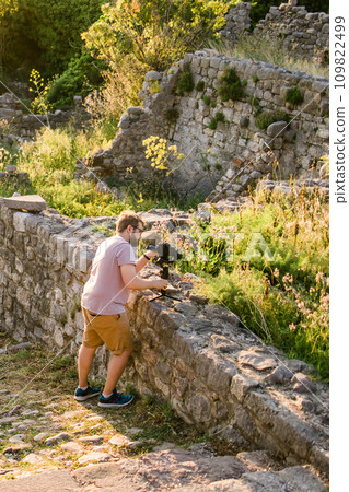 Cameraman in summer outfit with gimbal and cinema camera in his hands making travel video with old Europe Balkan nature and town on the background 109822499