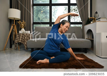 Active senior woman doing stretching exercise in living room. Domestic fitness concept Active senior woman doing stretching exercise in living room. Domestic fitness concept 109823035