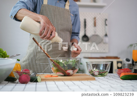 Hand of senior man pouring dressing into bowl with fresh salad on table. Hand of senior man pouring dressing into bowl with fresh salad on table. 109823239