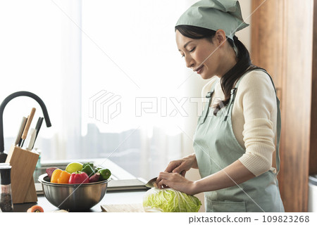 A woman in an apron cutting Chinese cabbage with a knife 109823268