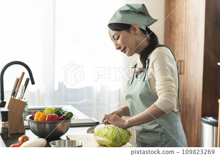 A woman in an apron cutting Chinese cabbage with a knife 109823269