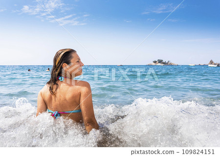Attractive woman in bikini sitting on the beach and being splashed by the waves 109824151