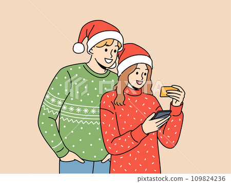 Couple in christmas clothes makes purchases on phone mobile app and uses credit card to pay 109824236