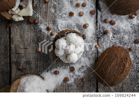 Coconut candy, balls, coconuts and hazelnuts on a rustic wooden surface 109824244