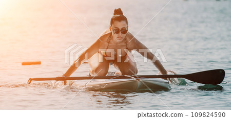 Sea woman sup. Silhouette of happy middle aged tanned woman in rainbow bikini, surfing on SUP board, confident paddling through water surface. Idyllic sunset. Active lifestyle at sea or river. 109824590