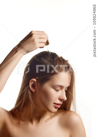 Portrait of attractive woman with long brunette hair applying vitaminized moisturizing oil for scalp against white background. 109824868