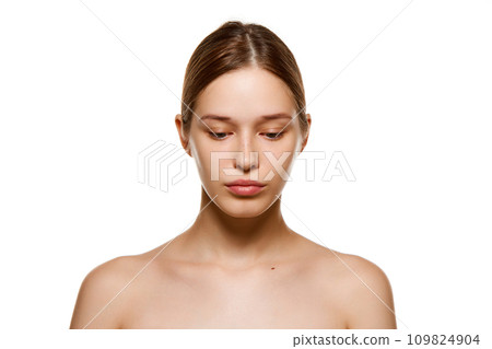 Portrait of beautiful young girl with bare shoulders, well-kept spotless skin looking down isolated white studio background Portrait of beautiful young girl with bare shoulders, well-kept spotless skin looking down isolated white studio background 109824904