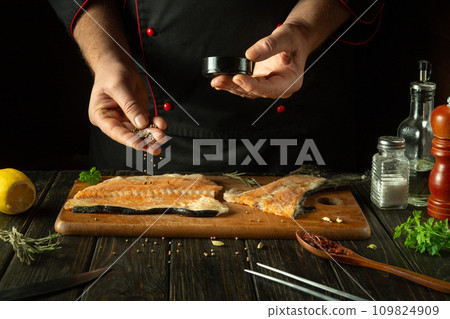 The chef adds coriander to the fish steak before salting it. Concept of preparing a fish dish on a kitchen table in a restaurant The chef adds coriander to the fish steak before salting it. Concept of preparing a fish dish on a kitchen table in a restaurant 109824909