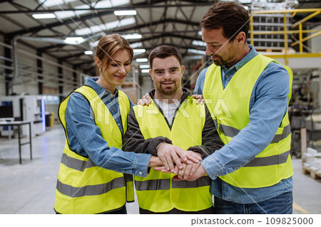 Portrait of young man with Down syndrome and his colleagues working in warehouse, holding hands as one team. Concept of workers with disabilities, support in workplace. Portrait of young man with Down syndrome and his colleagues working in warehouse, holding hands as one team. Concept of workers with disabilities, support in workplace. 109825000