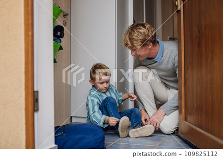 Boy getting ready for school, putting on shoes, getting dressed. Father taking son to school, kindergarten before going to work. Boy getting ready for school, putting on shoes, getting dressed. Father taking son to school, kindergarten before going to work. 109825112