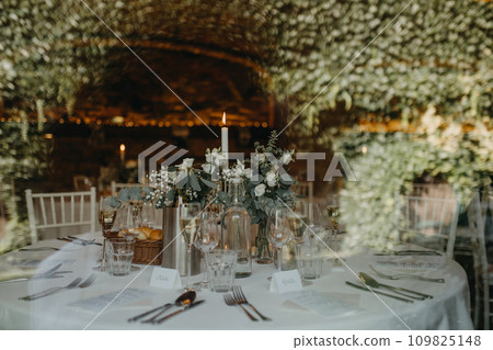 Elegant, romantic table setting for indoor wedding reception with fairy lights on wall behind. Luxury wedding table decoration, special event table set up with fresh flowers arragements. Elegant, romantic table setting for indoor wedding reception with fairy lights on wall behind. Luxury wedding table decoration, special event table set up with fresh flowers arragements. 109825148