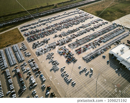 Aerial view of a massive parking lot at a car manufacturing facility with newly produced vehicles parked in rows. Aerial view of a massive parking lot at a car manufacturing facility with newly produced vehicles parked in rows. 109825192