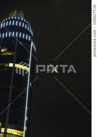 A jetliner overflies a scyscraper at night, minutes before landing in London, England A jetliner overflies a scyscraper at night, minutes before landing in London, England 109827516