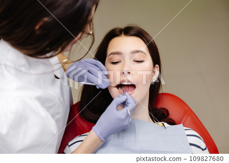 Portrait of smiling caucasian lady and cropped dentist hands in blue gloves with tools in hands Portrait of smiling caucasian lady and cropped dentist hands in blue gloves with tools in hands 109827680