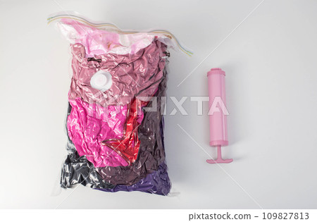 Pink hand pump for pumping air out of a bag with things on a white background. Modern technology for compact storage of things and clothes. 109827813
