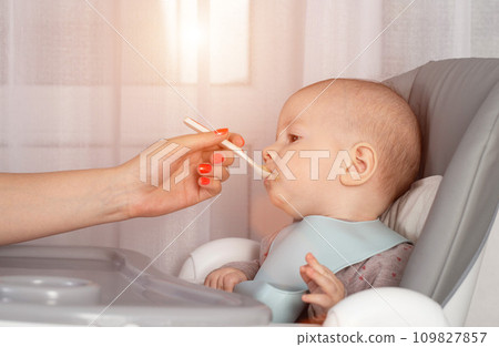 Feeding porridge and puree of a small child from a spoon. First meal. Copy space for text 109827857