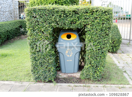 Gray plastic bin for glass bottle hide in shrub in garden. Gray plastic bin for glass bottle hide in shrub in garden. 109828867