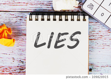 Lies word written on a sheet of notebook lying on old vintage boards with a calculator and folded paper Lies word written on a sheet of notebook lying on old vintage boards with a calculator and folded paper 109828915