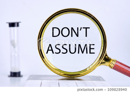 DO NOT ASSUME text, word, inscription found through a magnifying glass next to an hourglass on a light background DO NOT ASSUME text, word, inscription found through a magnifying glass next to an hourglass on a light background 109828940